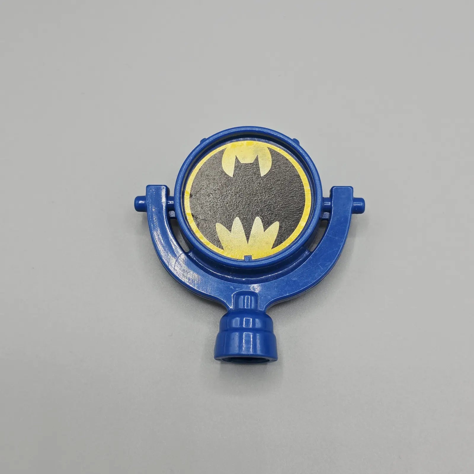 Blue plastic object with Batman logo on a gray background