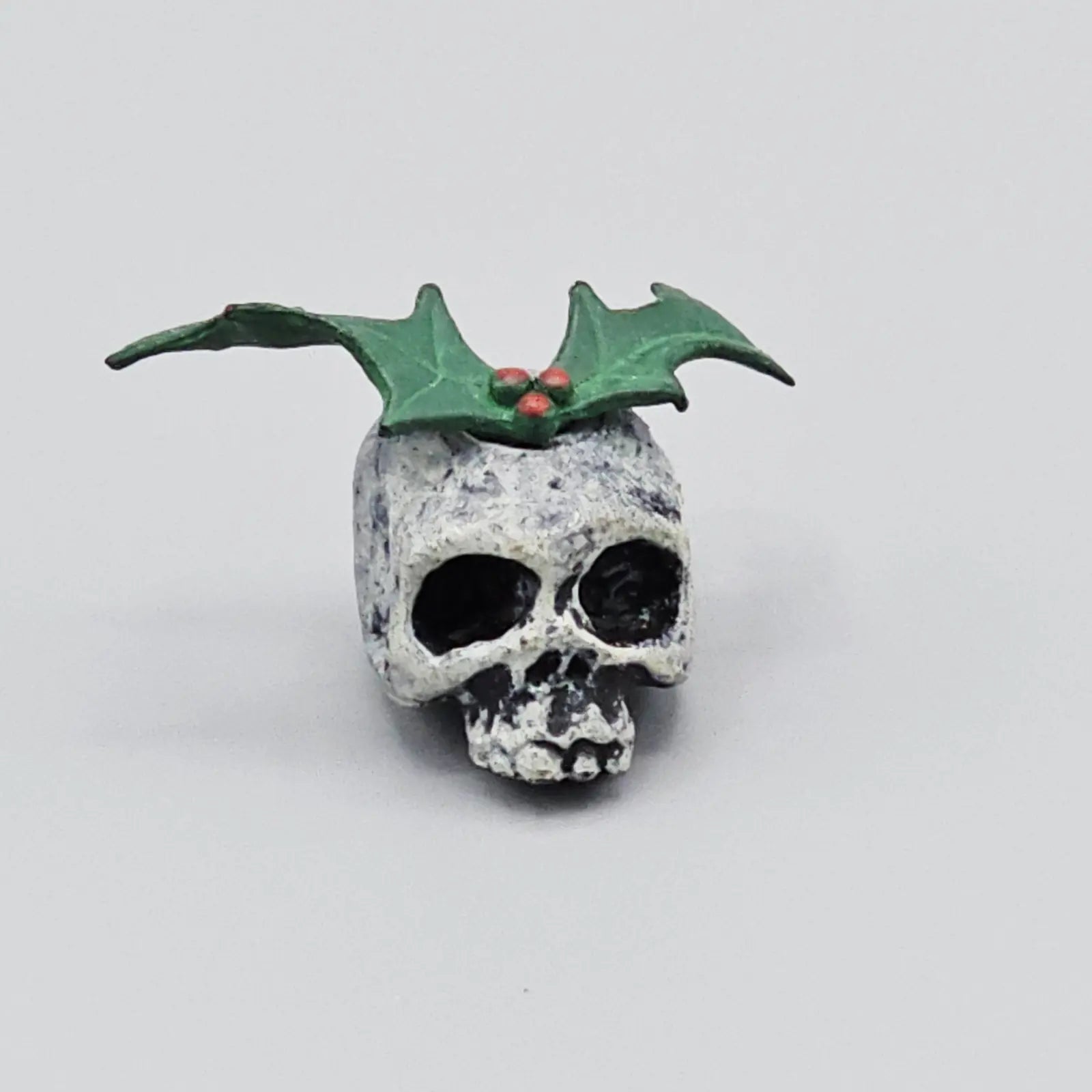 Skull with green leaves and red berries on a light gray background