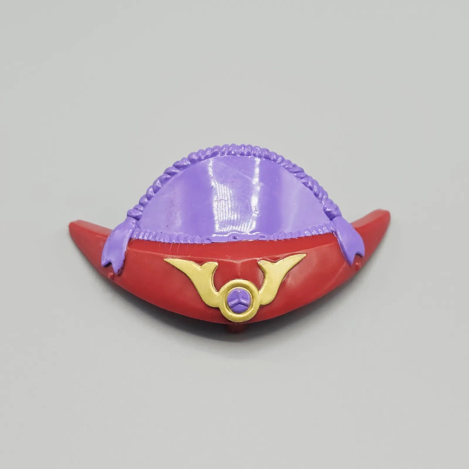 Toy helmet with red base, purple top, and gold emblem on a gray background